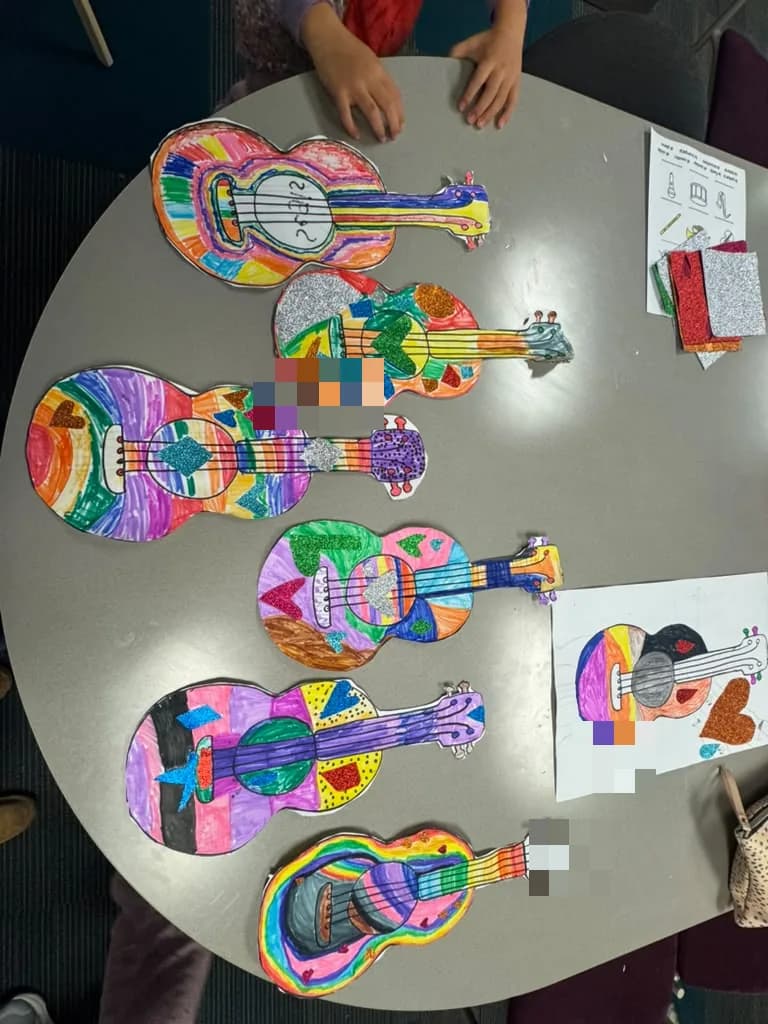 Paper guitars decorated with markers and glitter foam, spread across a classroom table
