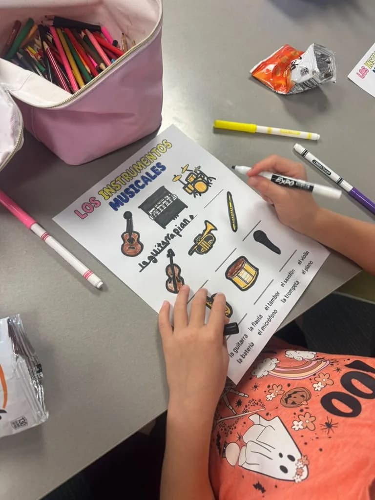 A child's hands colouring a worksheet of musical instruments, markers scattered on the table