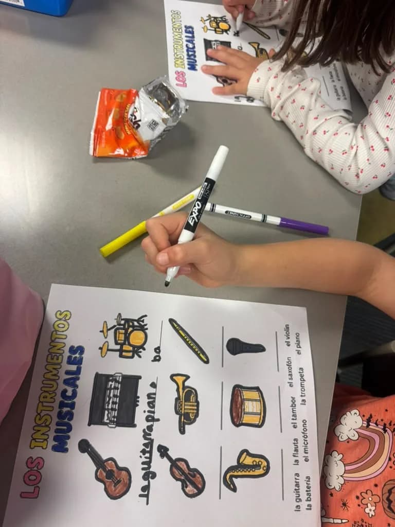 Two students working side by side on musical instrument worksheets with markers and a snack on the table