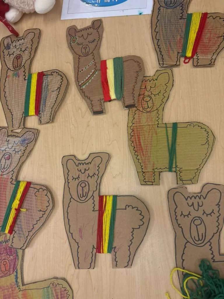 Close view of cardboard llamas with woven yarn blankets in red, yellow and green