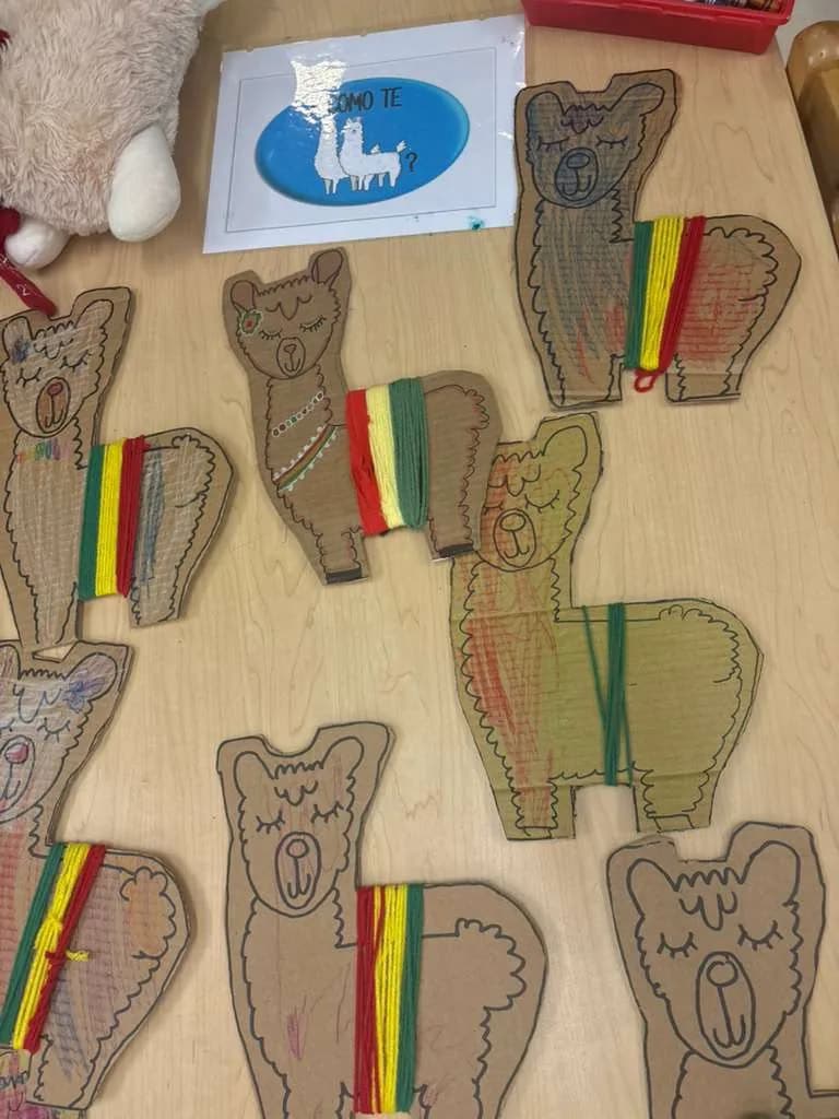 Cardboard llamas decorated with coloured yarn laid out on a classroom table