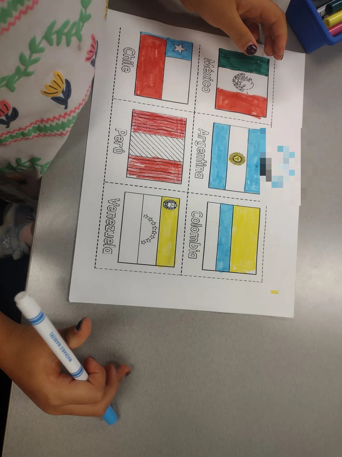 A child's hands colouring in a worksheet of South American flags with markers