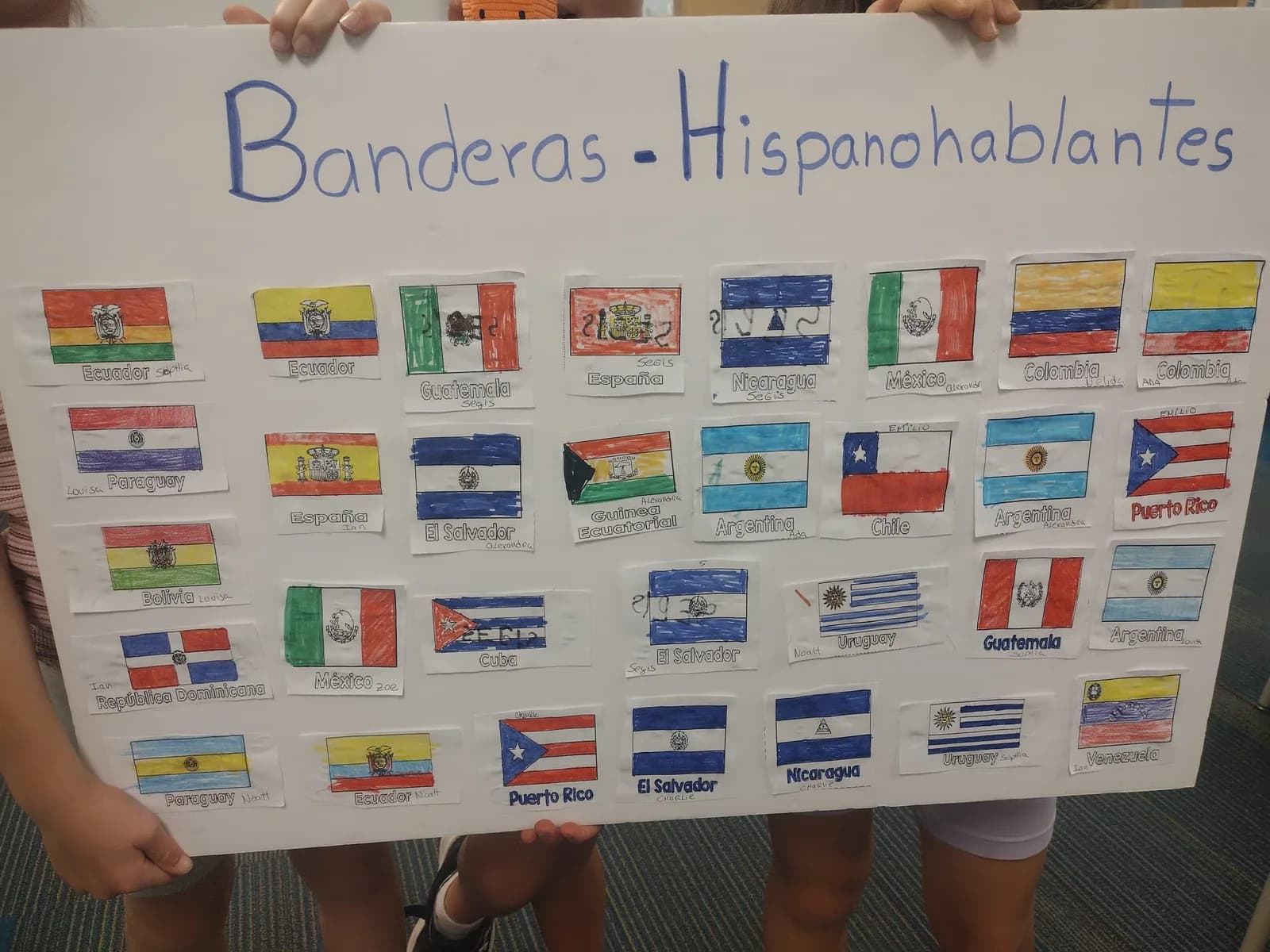 Students holding a poster of Spanish-speaking flags in a school hallway